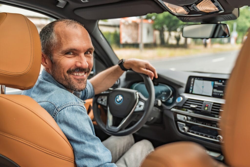 Mann auf Fahrersitz im Auto schaut lächelnd über die Schulter nach hinten