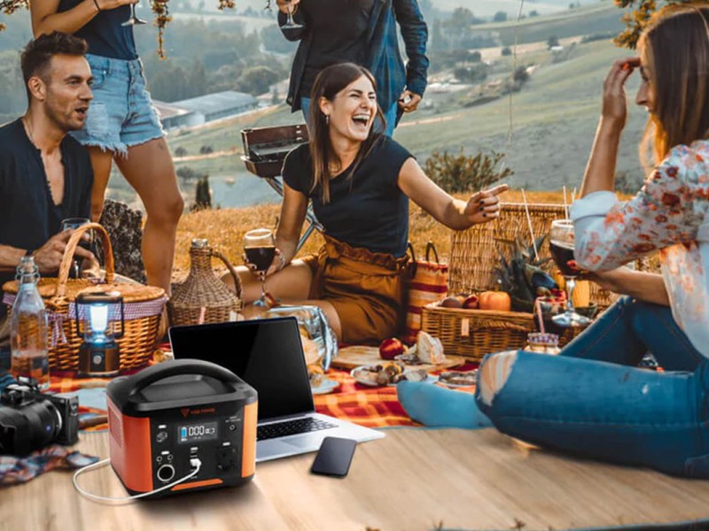 Mehrere Personen sitzen bei einem Picknick zusammen. Die Yose Powerstation lädt derweil einen Laptop auf.