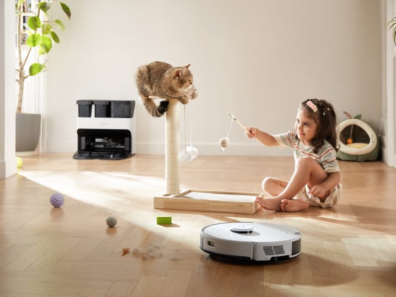 In der Mitte eines Raumes befinden sich ein Katzenbaum, auf dem eine Katze sitzt, mit der ein Kind spielt. Daneben der Roborock S7 Pro Ultra, der rund um die Szenerie sauber macht und putzt.