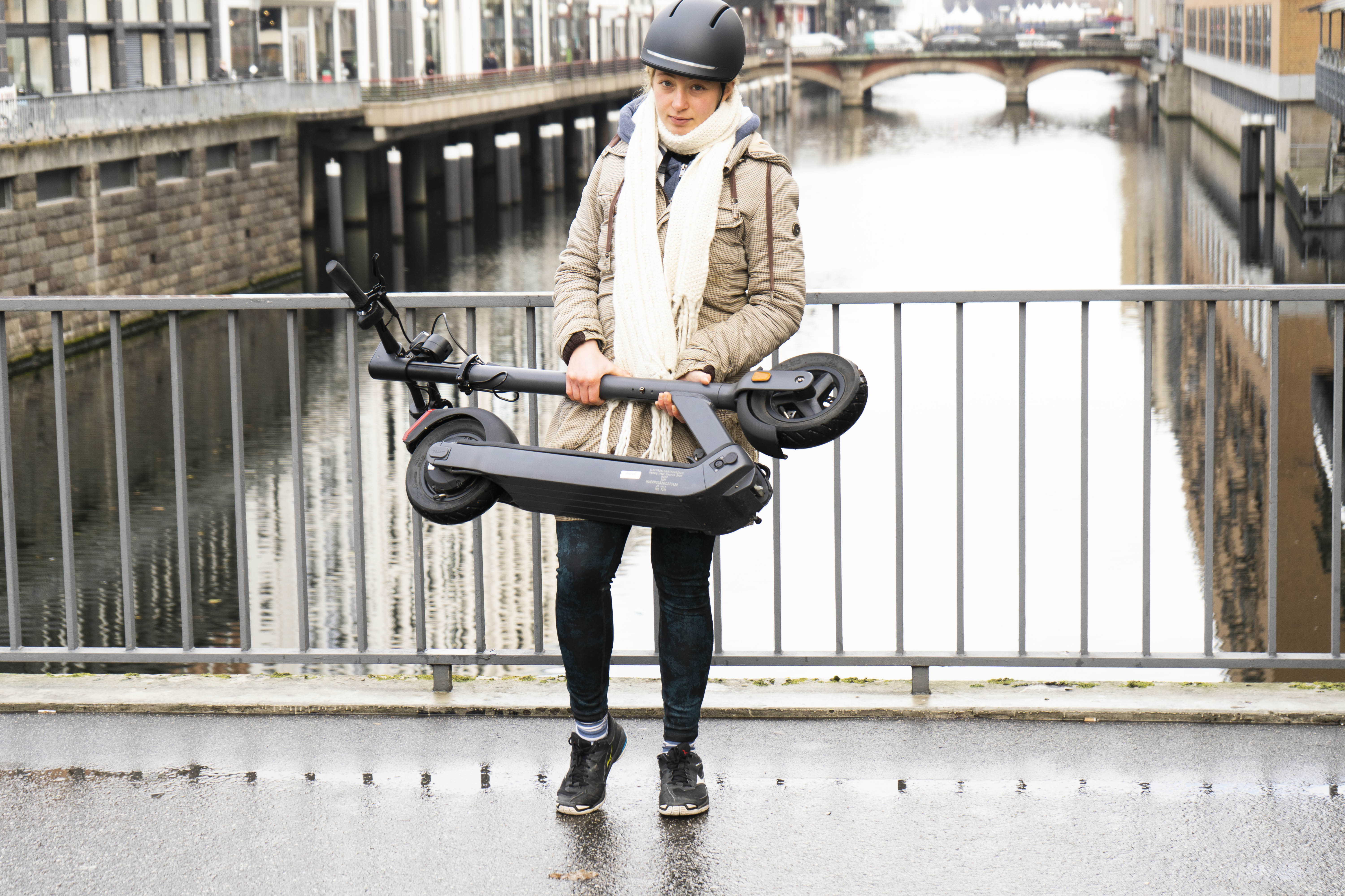 Eine junge Frau habt den zusammengeklappten Egret Pro E-Scooter.