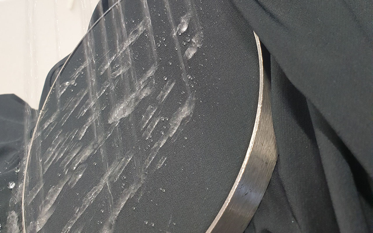 Detailbild: Softshell-Jacke wird im Labor mit Wasser besprüht.