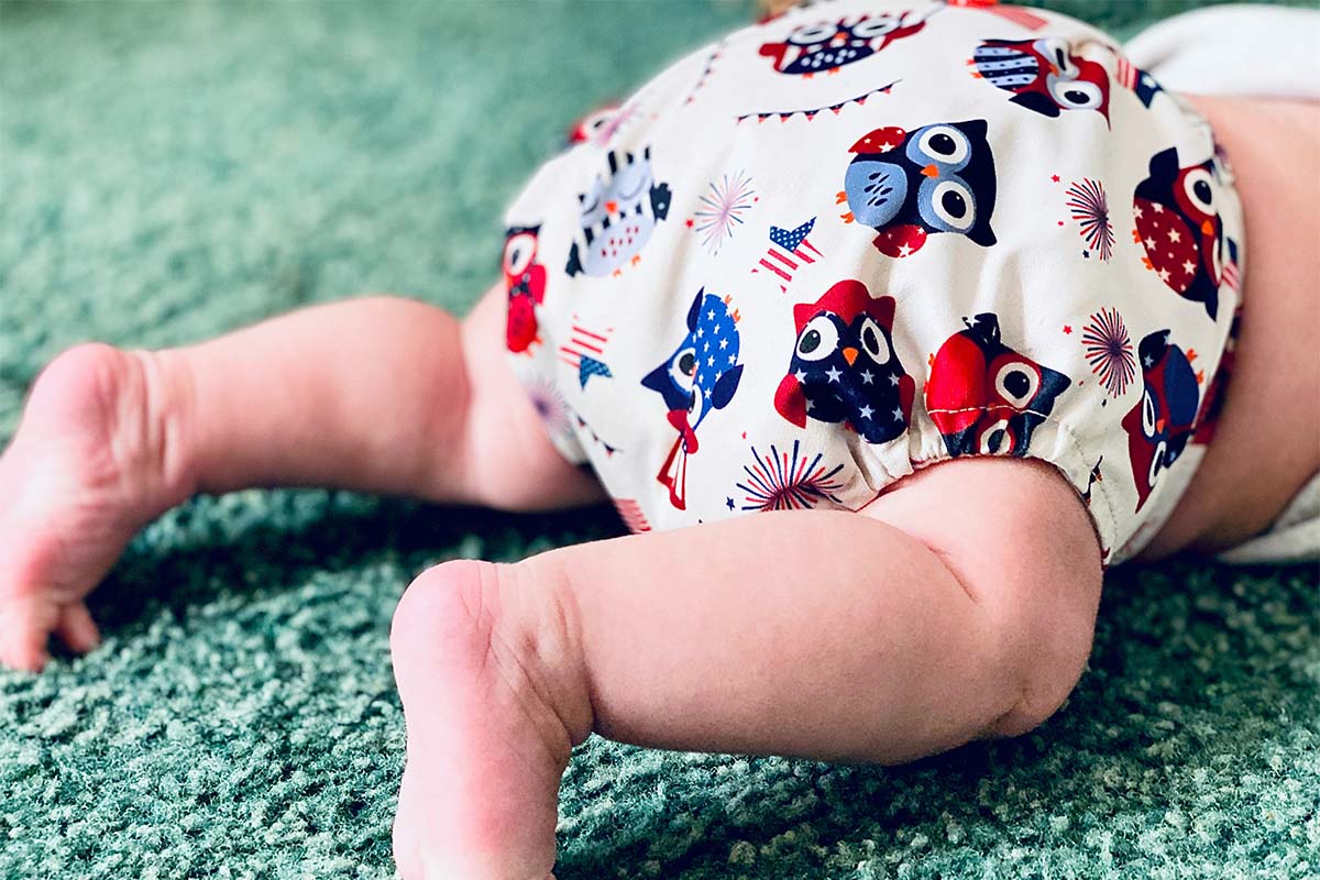 Nahaufnahme eines Babys, das man bauchabwärts auf dem Bauch liegend sieht, es trägt eine Windel mit Eulenmuster
