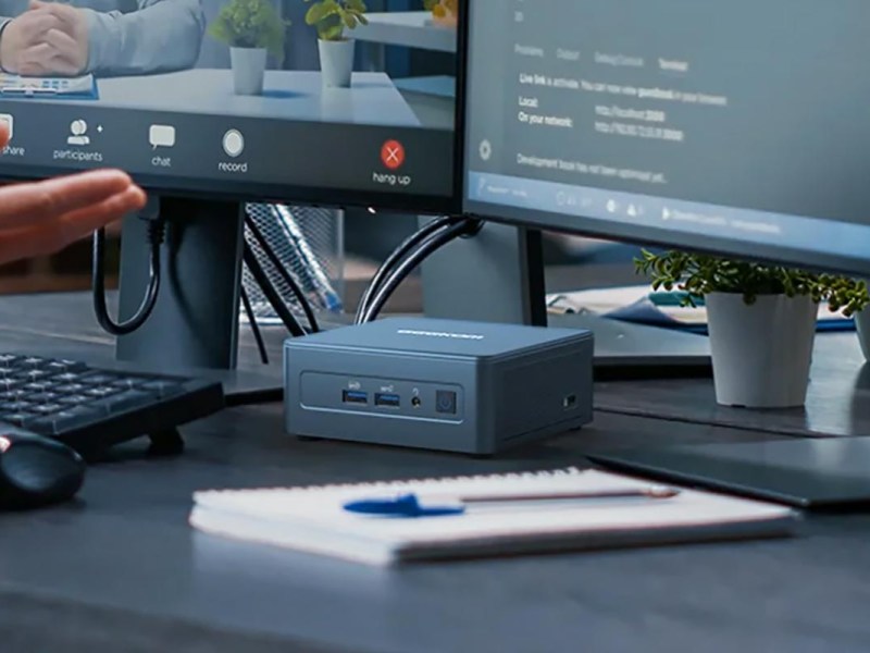 Mini-PC unter Monitoren auf einem Tisch.
