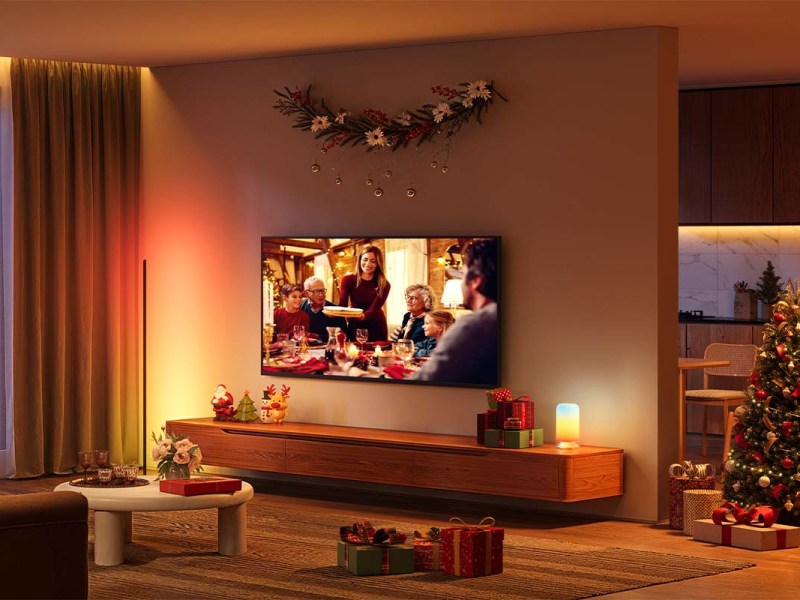Stimmungsvoll beleuchtetes Wohnzimmer, man sieht einen Fernseher, daneben einen geschmückten Weihnachtsbaum