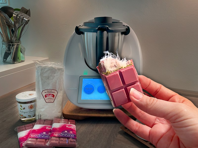 Eine Hand hält Angel Hair Schokolade hoch, im Hintergrund ein Thermomix und Zutaten.